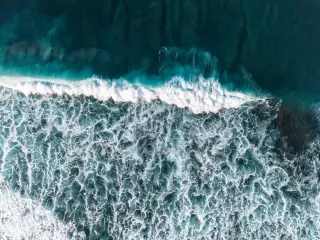 Ilustrasi: Pemandangan udara ombak laut berbusa putih memecah di perairan biru gelap.
