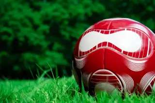 Ilustrasi: Sebuah bola sepak berwarna merah dan putih tergeletak di atas rumput hijau.