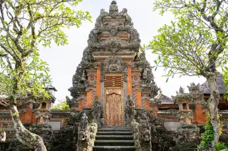 Ilustrasi: Gerbang kori agung pura khas Bali dengan ukiran batu dan pintu kayu berornamen emas.