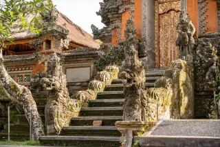 Ilustrasi: Tangga pura khas Bali dengan ukiran patung naga dan pintu kayu berukir emas.