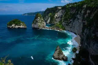 Ilustrasi: Pemandangan tebing tinggi di tepi pantai berpasir putih dan laut biru kehijauan.
