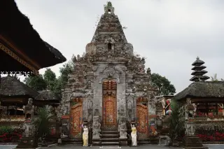 Ilustrasi: Gerbang kori agung berukir batu khas pura di Bali diapit arca dan pintu berukir emas.
