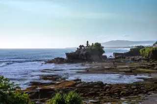 Ilustrasi: Pemandangan Pura Tanah Lot di atas bongkahan batu karang pesisir pantai dengan ombak laut.
