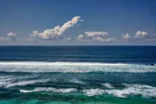 Ilustrasi: Hamparan laut biru berombak di bawah langit biru dengan awan putih di cakrawala.