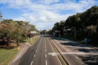 Ilustrasi: Jalan raya multijalur yang lengang diapit pepohonan hijau di bawah langit berawan.