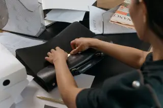 Ilustrasi: Seseorang membuka tas kerja kulit di atas meja kantor yang penuh dengan kertas dan dokumen.