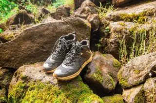 Ilustrasi: Sepasang sepatu mendaki diletakkan di atas bebatuan berlumut di alam terbuka.
