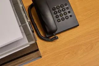 Ilustrasi: Telepon meja berwarna hitam dan baki dokumen di atas meja kayu.