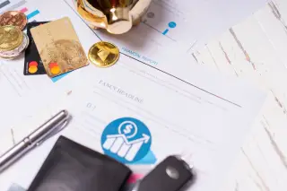 Ilustrasi: Laporan keuangan, koin kripto, kartu kredit, dompet, dan pena di atas meja putih.