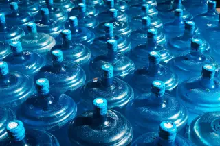 Ilustrasi: Deretan galon air minum berwarna biru tersusun rapi di bawah sinar matahari.