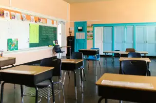 Ilustrasi: Ruang kelas kosong dengan jajaran meja dan kursi kayu serta papan tulis.