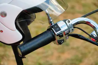 Ilustrasi: Setang sepeda motor dengan helm putih tergantung di spion.