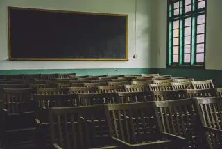Ilustrasi: Deretan kursi kayu di dalam ruang kelas kosong dengan papan tulis hitam di dinding.