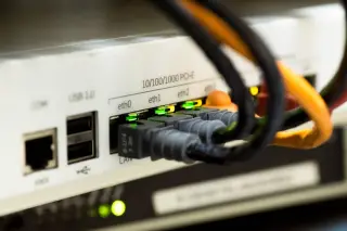 Ilustrasi: Kabel jaringan dan porta ethernet pada perangkat router dengan lampu indikator menyala.