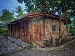 Ilustrasi: Rumah kayu tradisional sederhana dengan atap genting di pedesaan.