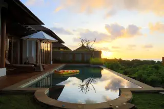 Ilustrasi: Kolam renang di vila dengan pemandangan pepohonan hijau saat matahari terbenam.