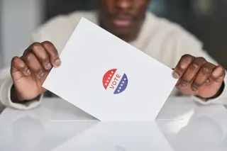 Ilustrasi: Seseorang memasukkan surat suara bertuliskan kata VOTE ke dalam celah kotak suara putih.
