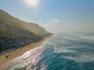 Ilustrasi: Pemandangan udara garis pantai berpasir dengan ombak laut dan tebing hijau di bawah sinar matahari.
