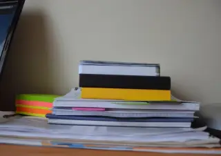 Ilustrasi: Tumpukan buku catatan, kertas berkas, dan sticky notes di atas meja.