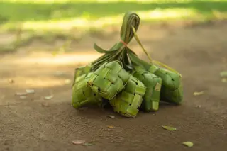 Ilustrasi: Seikat anyaman ketupat daun kelapa hijau diletakkan di atas tanah berpasir.
