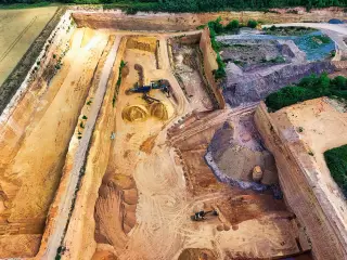Ilustrasi: Pemandangan udara area tambang galian terbuka dengan tumpukan pasir dan alat berat.