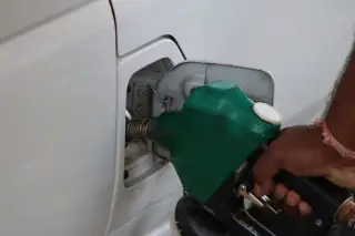 Ilustrasi: Tangan seseorang memegang nozel bahan bakar hijau untuk mengisi tangki mobil putih.