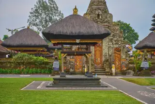 Ilustrasi: Bangunan bale dan gerbang pura khas Bali di area pelataran berumput.