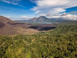 Ilustrasi: Pemandangan lanskap kaldera gunung berapi dengan danau dan hutan di bawah langit berawan.