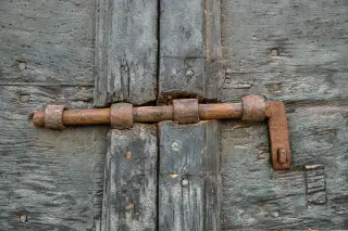 Ilustrasi: Palang besi berkarat yang mengunci pintu kayu tua yang lapuk.