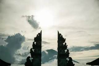Ilustrasi: Siluet candi bentar dengan latar belakang gunung berawan di bawah sinar matahari.