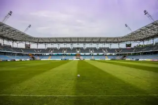 Ilustrasi: Sebuah bola sepak berada di tengah lapangan rumput stadion kosong beratap baja.