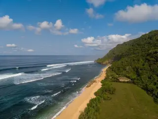 Ilustrasi: Pemandangan udara pesisir pantai berpasir dengan tebing hijau dan langit biru berawan.