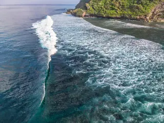 Ilustrasi: Pemandangan udara ombak laut besar berbusa putih menuju tebing pantai berkarang.