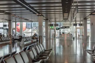Ilustrasi: Area ruang tunggu keberangkatan bandara dengan deretan kursi dan pesawat di luar jendela.