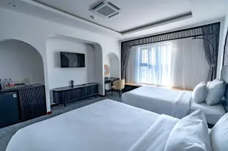 Ilustrasi: Kamar hotel modern bernuansa putih dengan dua tempat tidur, televisi di dinding, dan jendela bertirai tipis.