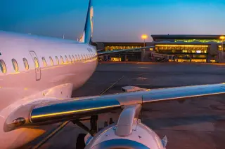 Ilustrasi: Pesawat komersial terparkir di apron bandara dengan latar terminal bercahaya di waktu senja.