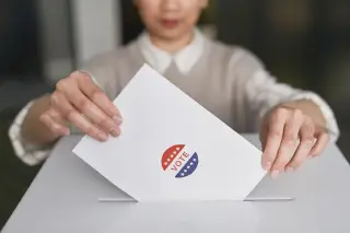 Ilustrasi: Seseorang memasukkan amplop bertuliskan vote ke dalam celah kotak suara putih.