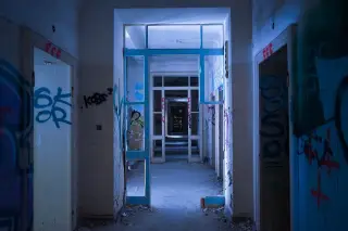 Ilustrasi: Lorong bangunan kosong dengan dinding bernoda grafiti dan pintu kaca yang rusak.