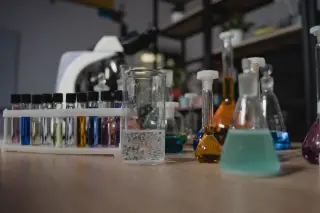Ilustrasi: Tabung reaksi dan labu ukur berisi cairan warna-warni di atas meja laboratorium.