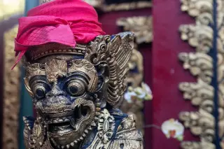 Ilustrasi: Patung ukiran tradisional Bali berhias kain merah di kepalanya.