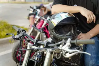 Ilustrasi: Helm bertengger di atas tangki motor di samping seorang pengendara.