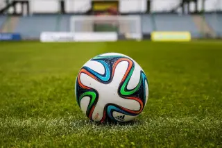 Ilustrasi: Sebuah bola sepak bermotif warna-warni tergeletak di atas rumput hijau di stadion.