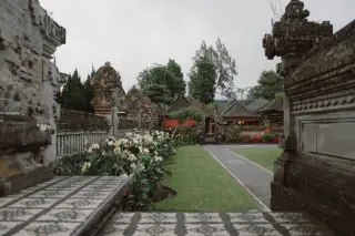 Ilustrasi: Kompleks pelataran pura tradisional Bali dengan taman bunga dan tembok berukir.