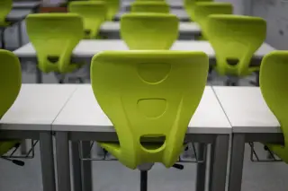 Ilustrasi: Deretan kursi plastik hijau dan meja putih di dalam ruang kelas kosong.