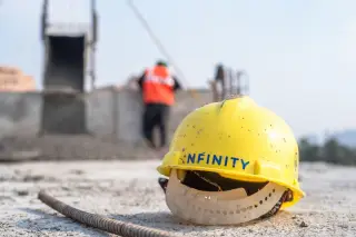Ilustrasi: Helm proyek kuning di tanah dengan latar belakang buram pekerja konstruksi.