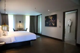 Ilustrasi: Kamar hotel modern yang luas dengan tempat tidur rapi, lampu gantung, dan pintu kamar mandi terbuka.