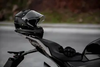 Ilustrasi: Helm hitam diletakkan di bagian belakang sepeda motor di tepi jalan.