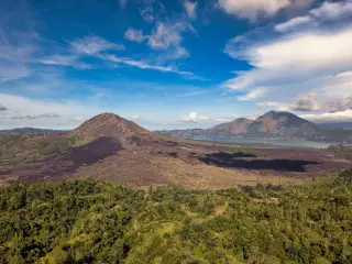 Ilustrasi: Pemandangan udara Gunung Batur dan Danau Batur di bawah langit biru berawan.