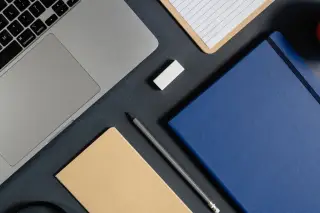 Ilustrasi: Tampak atas meja kerja dengan laptop, buku catatan, dan alat tulis tertata rapi.