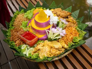 Ilustrasi: Sajian nasi tumpeng kuning lengkap dengan lauk-pauk di atas tampah bambu beralaskan daun pisang.